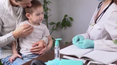 Genç bir bayan doktor, elektronik termometre kullanarak küçük bir çocuğun hasta sıcaklığını ölçüyor.