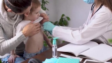 Genç bir bayan doktor, elektronik termometre kullanarak küçük bir çocuğun hasta sıcaklığını ölçüyor.