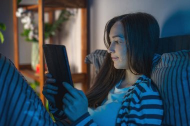 Karanlık bir yatak odasında genç bir kadın gece geç saatlerde yatağında yatıyor ve tabletini internette sörf yapmak ya da elektronik kitap okumak için kullanıyor. Uyku zamanı eğlencesi ve uykusuzluk kavramı.