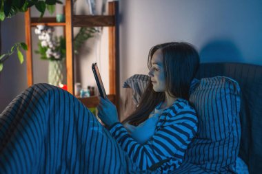 Karanlık bir yatak odasında genç bir kadın gece geç saatlerde yatağında yatıyor ve tabletini internette sörf yapmak ya da elektronik kitap okumak için kullanıyor. Uyku zamanı eğlencesi ve uykusuzluk kavramı.