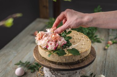 Dekoratörün eli lezzetli çiğ kremalı pastayı şefkat pembe çiçeklerle süslüyor. Romantik ruh hali ve bahar atmosferi kavramı.