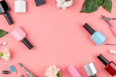 Pembe arka planda manikür ve pedikür için renkli oje şişeleri, aletler ve aksesuarlar. Üst görünüm ve kopyalama alanı.