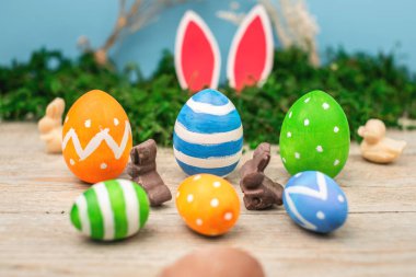 Parlak renkli Paskalya yumurtaları ve yeşil yosunlu mavi ve ahşap arka planda tavşan kulakları..