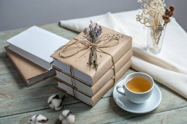İpe sarılı, lavanta çiçekleriyle süslenmiş ve ahşap bir masanın üzerinde bir fincan çay bulunan şirin kitap yığını. Kitap okumak ve kutlamak için rahat bir ortam kavramı.