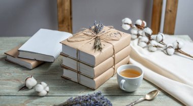 İple sarılmış, lavanta çiçekleriyle süslenmiş ve ahşap bir masada bir fincan çayla süslenmiş, el işi kağıt kapaklı güzel bir kitap yığını. Okumak için rahat bir atmosfer kavramı.