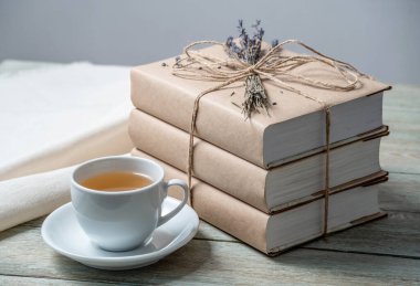 İpe sarılı, lavanta çiçekleriyle süslenmiş ve ahşap bir masada bir fincan çayla süslenmiş rahat kitap yığını. Okumak için rahat bir atmosfer kavramı.