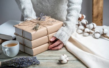 Kadınların elleri, iple sarılmış ve lavanta ile süslenmiş el işi kağıt kılıflarında kitap yığınını dikkatle tutar..