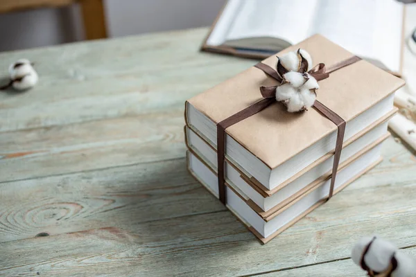 Stack of beautifully wrapped craft paper books, tied with ribbon and decorated with cotton, on a wooden table. Concept of reading and books as a gift. Copy space.