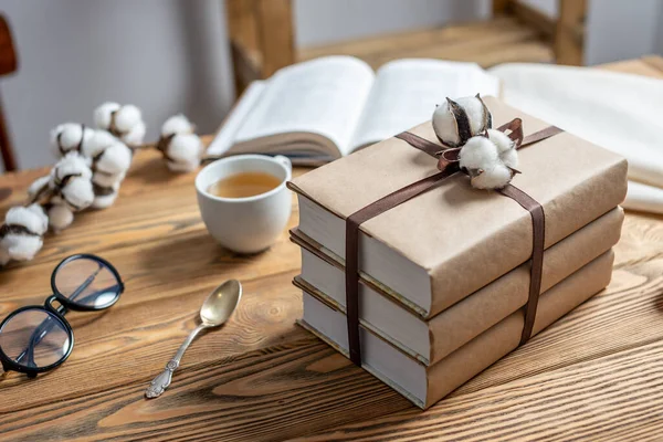 A stack of beautifully wrapped craft paper books, tied with ribbon and decorated with cotton, on a wooden table. Concept of reading and books as a gift.