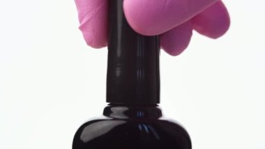 El mor bir oje şişesini indiriyor, kapağı açıyor, bir damla vernikle fırçayı çekiyor ve tutarlılığını ve rengini gösteriyor. Beyaz arkaplan ve yakın plan