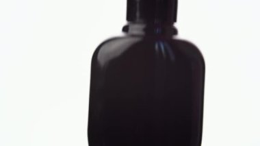 Eldivenli bir el, bir şişe kırmızı oje koyuyor, kapağı söküyor, bir damla vernikle bir fırça çekiyor ve tutarlılığını ve rengini gösteriyor. Beyaz arkaplan ve yakın plan