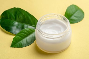 Krema ve yeşil yapraklar, fotokopi alanı olan sarı bir masanın üzerinde. Cilt bakımı kavramı ve doğal organik bileşim ile kozmetik kullanımı.