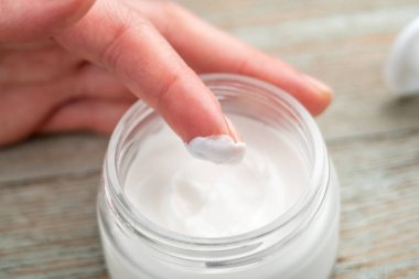 Bir kadının eli, parmağıyla kavanozdan krem alıyor. Cilt bakımı kavramı ve doğal bir bileşimle kozmetik kullanımı. Yakın çekim..