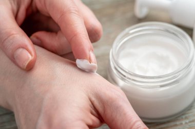 Kadının eli, diğer eline kavanozdan organik krem sürmek için parmağını kullanıyor. Cilt bakımı kavramı ve doğal bir bileşimle kozmetik kullanımı.