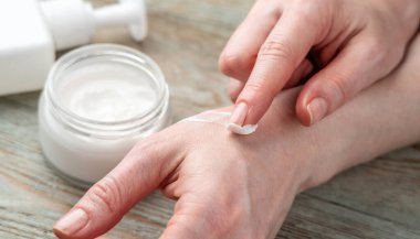 Kadının eli, diğer eline kavanozdan organik krem sürmek için parmağını kullanıyor. Cilt bakımı kavramı ve doğal bir bileşimle kozmetik kullanımı.