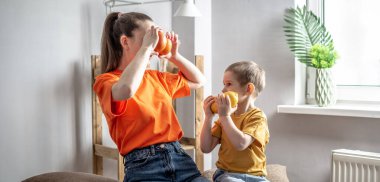 Neşeli anne ve oğul şakalaşıyor, birlikte gülüp oynuyorlar, gözlerine meyve koyuyorlar. Mutlu ve sağlıklı bir aile kavramı, çocuklarla zaman geçirme..