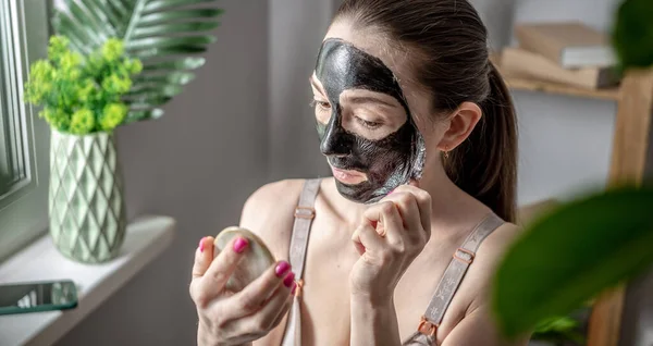 Młoda Kobieta Trzyma Lustro Ręku Zdejmuje Kosmetyczną Czarną Maskę Twarzy — Zdjęcie stockowe