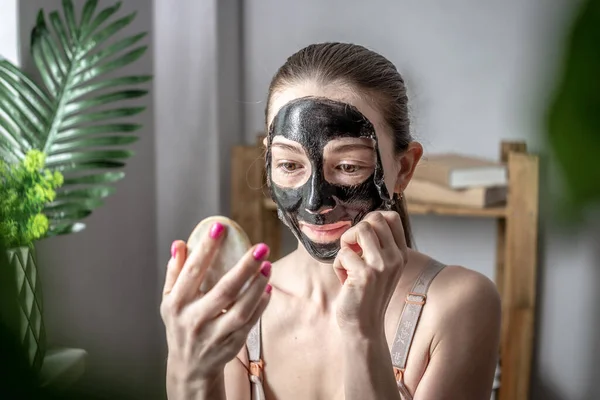 Młoda Piękna Kobieta Trzyma Lustro Ręku Zdejmuje Kosmetyczną Czarną Maskę — Zdjęcie stockowe