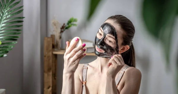 Młoda Kobieta Trzyma Lustro Ręku Zdejmuje Kosmetyczną Czarną Maskę Twarzy — Zdjęcie stockowe