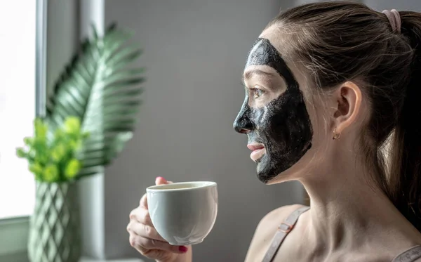 Młoda Kobieta Naturalnej Kosmetycznej Czarnej Masce Twarzy Pije Kawę Pojęcie — Zdjęcie stockowe
