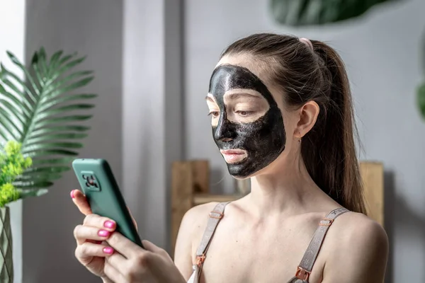 얼굴에 화장품용 마스크를 여자가 휴대폰을 사용하고 있습니다 전환의 — 스톡 사진