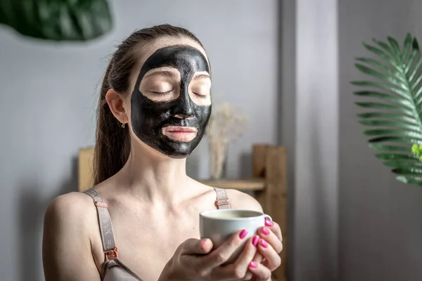 Młoda Kobieta Kosmetycznej Czarnej Masce Twarzy Filiżanką Kawy Pojęcie Pielęgnacji — Zdjęcie stockowe
