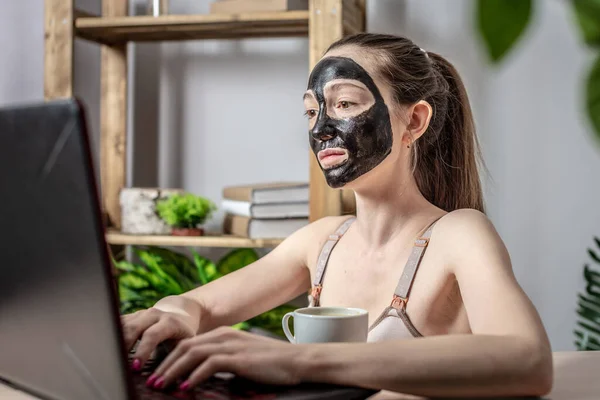Egy Fiatal Kozmetikai Fekete Maszkkal Arcán Egy Csésze Kávé Laptopot — Stock Fotó