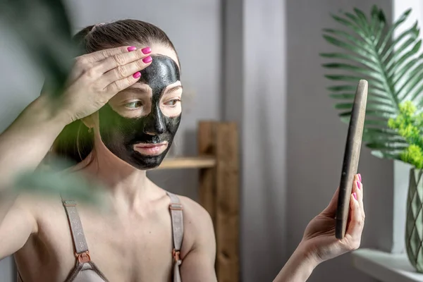 Jonge Vrouw Gebruikt Een Cosmetisch Zwart Gezichtsmasker Kijkt Spiegel Concept — Stockfoto