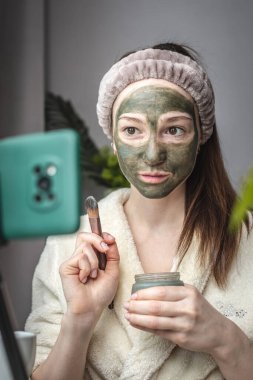 Bornozlu kadın blogcu, cep telefonu kamerasının önünde yüzüne yeşil bir maske takıyor..