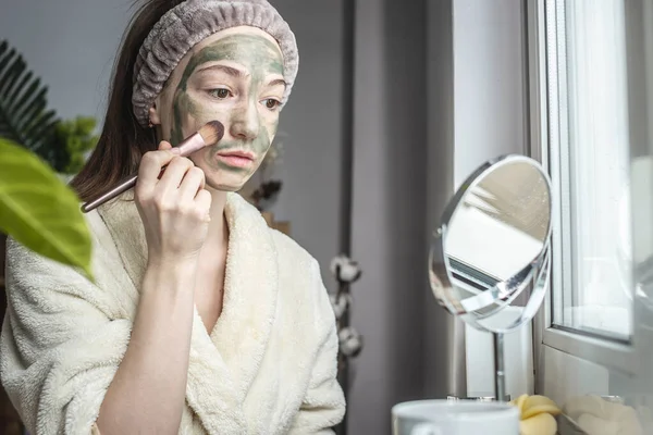 Egy Fiatal Csinos Egy Fürdőköpenyben Tükör Előtt Zöld Kozmetikai Maszkot — Stock Fotó