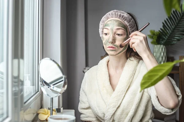 Egy Fiatal Csinos Egy Fürdőköpenyben Tükör Előtt Zöld Kozmetikai Maszkot — Stock Fotó