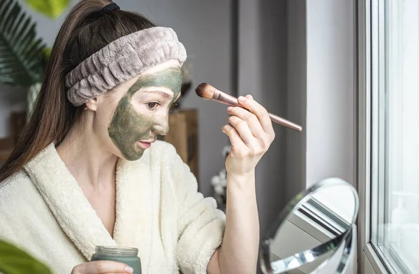 Egy Fiatal Csinos Fürdőköpenyben Zöld Kozmetikai Maszkot Visel Arcán Egy — Stock Fotó