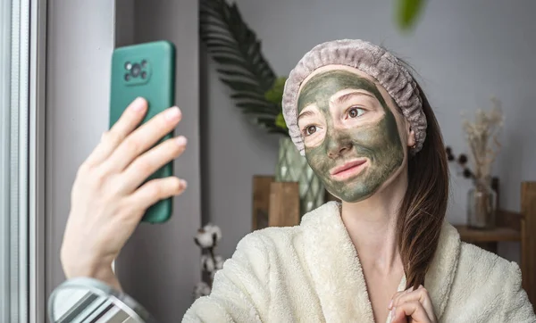 Młoda Piękna Kobieta Szlafroku Zieloną Maską Kosmetyczną Twarzy Robi Sobie — Zdjęcie stockowe