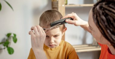 Genç, modern bir kadın kuaför bir çocuğun saçını makasla kesiyor. Çocuk memnun değil, bu işlemden hoşlanmıyor.