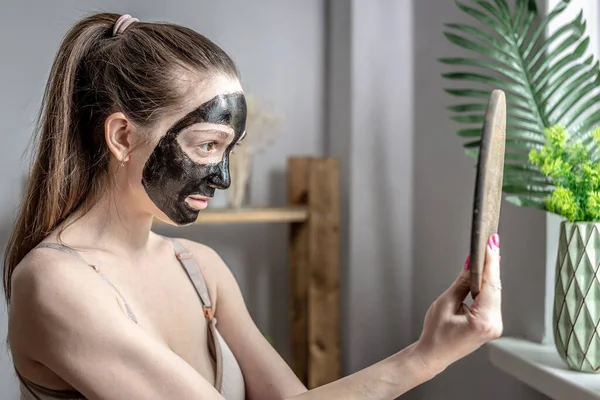 Jonge Vrouw Gebruikt Een Cosmetisch Zwart Gezichtsmasker Kijkt Spiegel Concept — Stockfoto