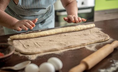 Mutfakta önlüklü bir kadın lezzetli ev yapımı tarçınlı çörekler yapmak için taze çiğ hamuru nazikçe büküyor. Pişirme süreci kavramı.