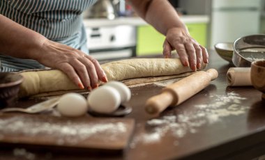 Mutfakta önlüklü bir kadın lezzetli ev yapımı tarçınlı çörekler yapmak için taze çiğ hamuru nazikçe büküyor. Pişirme süreci kavramı.
