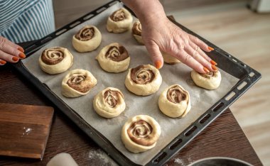 Kadınların elleri pişirmeden önce çiğ tarçınlı çörekleri kabın üzerine nazikçe koyuyorlar. Ev yapımı pişirme sürecinin kavramı.