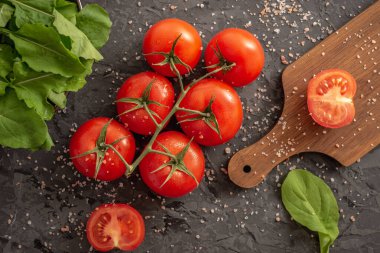 Domates, roka, yeşil salata ve siyah arka planda hafif sağlıklı sebze salatası pişirmek için kesim tahtası var. Üst görünüm.
