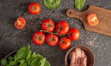 Domates, roka, yeşil salata ve siyah arka planda hafif sağlıklı sebze salatası pişirmek için kesim tahtası var. Üst görünüm.