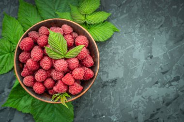 Siyah arka planda yeşil ahududu yapraklarıyla çevrili bir kasede lezzetli olgun ahududular. Boşluğu ve üst görünümü kopyala.