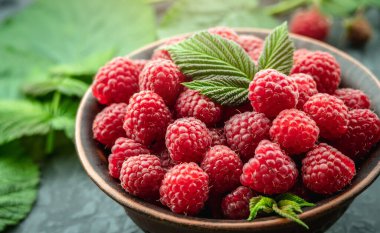 Taze olgun ahududular ve siyah arka planda yeşil yapraklarla dolu bir kase..