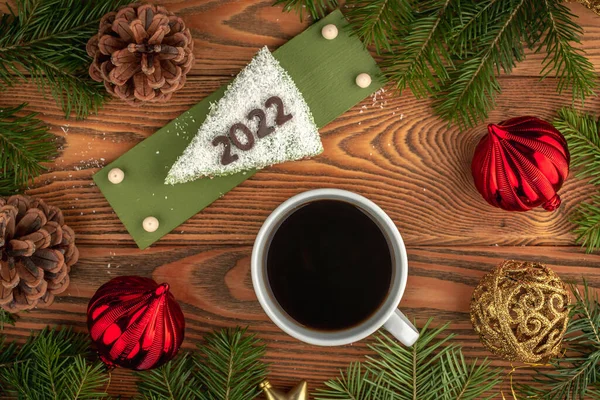 白いお祝いのケーキでコーヒーのカップは 針葉樹の枝やクリスマスのおもちゃで木製の背景にチョコレートで作られた数2022で飾られています トップ表示 — ストック写真