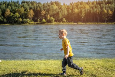 Ormanda nehir kıyısı boyunca koşan bir çocuk var. Doğa eğlencesi kavramı, aktif eğlence, boş zaman..