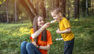 Mutlu anne ve çocuk kamp ateşinde kavruluyor ve şekerleme yiyorlar. Aile pikniği kavramı, doğada aktif eğlence, yaşam tarzı, boş zaman.