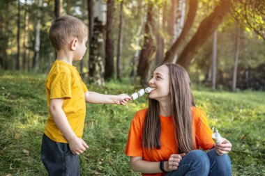 Mutlu anne ve çocuk kamp ateşinde kavruluyor ve şekerleme yiyorlar. Aile pikniği kavramı, doğada aktif eğlence, yaşam tarzı, boş zaman.