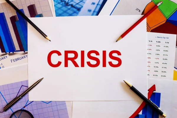 Слово Crisis Написано Белом Фоне Рядом Цветными Графиками Ручками Карандашами — стоковое фото