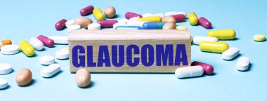 GLAUCOMA sözcüğünün bulunduğu tahta blok çok renkli haplar arasında mavi bir arkaplanda duruyor. Tıbbi konsept
