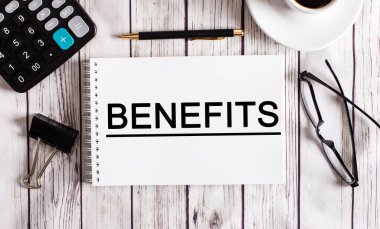 BENEFITS kelimesi bir hesap makinesinin, kahvenin, bardakların ve kalemin yanında beyaz bir not defterine yazılmıştır. İş konsepti