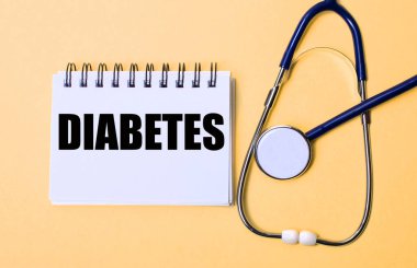 Bej bir arka planda, steteskop ve diyabet yazılı beyaz bir not defteri. Tıbbi konsept